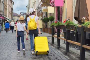 Two girls walking in city with suitcase, back view