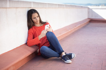 Chica adolescente mirando el smartphone sentada en la azotea