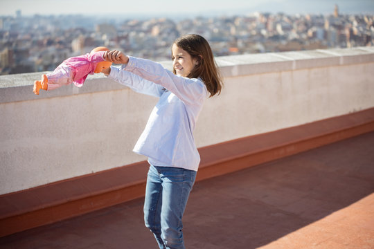 Ni&ntilde;a de pie jugando con una mu&ntilde;eca en la azotea