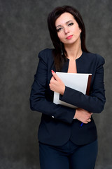 Naklejka premium Portrait of a brunette manager woman in a business suit on a gray background. Great makeup and beautiful hair. Standing right in front of the camera in various poses.