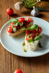 bruschetta with cherry tomatoes, basil, pesto sauce and mozzarella on a white plate on a wooden background. Italian restaurant. Top view food photo