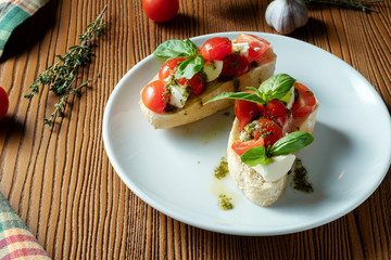 bruschetta with cherry tomatoes, basil, pesto sauce and mozzarella on a white plate on a wooden background. Italian restaurant. Top view food photo