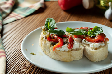 Fototapeta na wymiar bruschetta with bell pepper, basil, pesto sauce and mozzarella on a white plate on a wooden background. Italian restaurant. Top view food photo