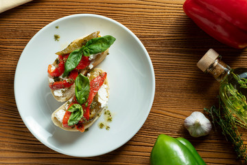 bruschetta with bell pepper, basil, pesto sauce and mozzarella on a white plate on a wooden background. Italian restaurant. Top view food photo