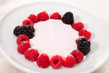 fresh raspberries and blackberries laid out on a white plate in circle with yogurt