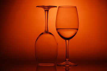 Two wine glasses on orange background. One glass upside down