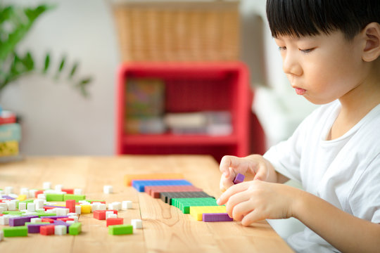 Cute kindergarten Asian boy learning about numeracy, adding - subtracting and counting through colorful cuisenaire rods. Early math, Cognitive skills, Problem solving, Child development, Education.