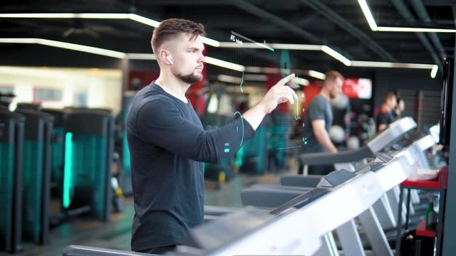 Gym, athlete walks on a treadmill and uses the futuristic hologram interface, tracking progress in sports, HUD, modern technology.