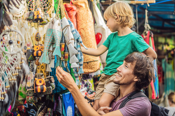 Dad and son at a market in Ubud, Bali. Typical souvenir shop selling souvenirs and handicrafts of Bali at the famous Ubud Market, Indonesia. Balinese market. Souvenirs of wood and crafts of local