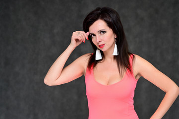 Portrait of a beautiful brunette woman in a coral t-shirt on a gray background. Stands in different poses with emotions. Great makeup and beautiful hair.