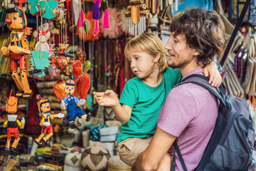 Dad and son at a market in Ubud, Bali. Typical souvenir shop selling souvenirs and handicrafts of Bali at the famous Ubud Market, Indonesia. Balinese market. Souvenirs of wood and crafts of local