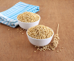 Sorghum, also known as jowar, which is a whole grain and a healthy food, in bowls, and its stalk, on a wooden background.