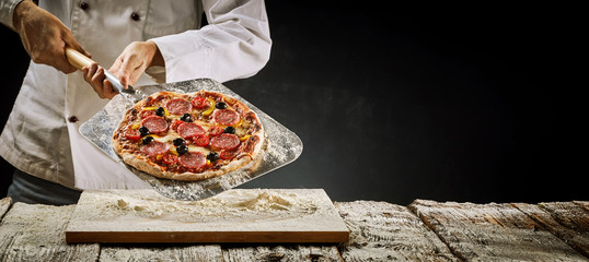 Chef removing a salami pizza from the oven - obrazy, fototapety, plakaty