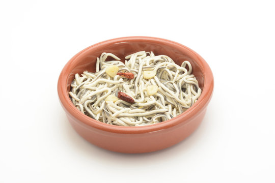 Gulas cocinadas con ajo y guindilla en una cazuela de barro sobre fondo blanco