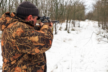Hunter with a sniper rifle in the winter forest. A man is looking for a target