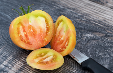 Big fresh yellow cut tomato with knife isolated on wood  background.