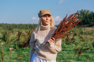 Happy beautiful blond woman walking in a green field with a bouquete of dry brown plants