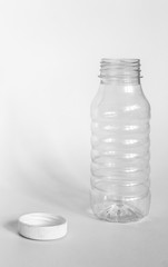 empty transparent open plastic bottle without cap, cap lies next to a white background, concept of debris removal