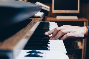 male musician, arranger, producer hand playing on piano keys in home studio