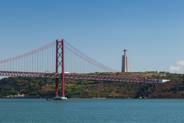 Tagus River, 25 de Abril Bridge (Ponte 25 de Abril, 25th of April Bridge) and Sanctuary of Christ the King (Santuario de Cristo Rei) monument in Lisbon, Portugal, on a sunny day.