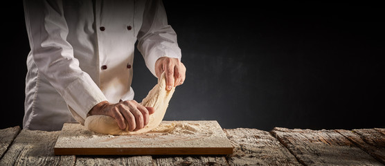 Hands of a male chef, cook or baker kneading dough - obrazy, fototapety, plakaty