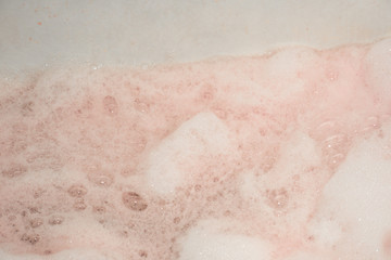 Fototapeta premium Soapy foam painted red in the bath is close