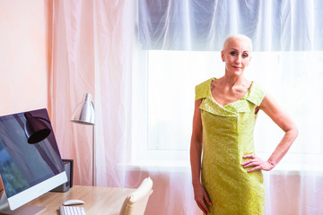 Senior Adults Concepts. Portrait of Tranquil Positive Caucasian Female Posing in Green Dress Indoors In Front of The Window.