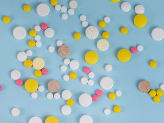 Bunch of multicolored tablets scattered on the surface on a blue background. The concept of medicine and healthcare.