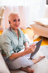 Seniors and Modern Technologies Concepts. Smiling Relaxing Caucasian Senior Woman Posing With Laptop And Listening To The Music on Couch Indoors.