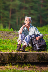 Portrait of Senior Woman With Tourist Backpack Dreaming in Forest Outdoors On Nature Background.