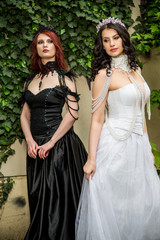Two Caucasian Models Posing Together Outdoors. Standing in Black and White Dresses. Wearing Tiara.