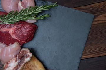 carnivore keto diet flat lay. beef steak, chicken breast and pork shank assorted meat near a board made of natural stone. what to eat on carnivore diet