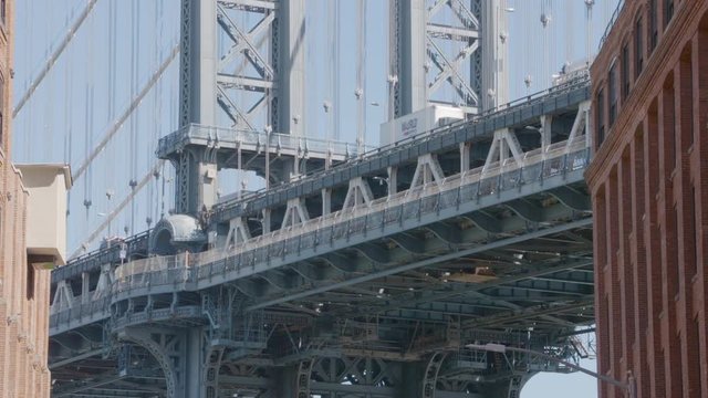 An upwards, long dolly shot of behind brookyln bridge from the ground with people sittting down around the hotfog cart, going upwards to the American flag posted ontop of the bridge. 