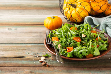 Delicious salad with arugula, baked pumpkin, hazelnut and sesame seeds on brown plate. Paleo diet food concept with copy space.