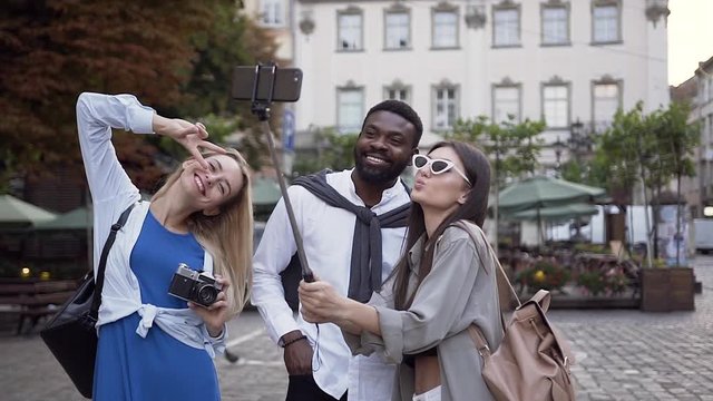Satisfied smiling multiracial friends making selfie in the cente of city street