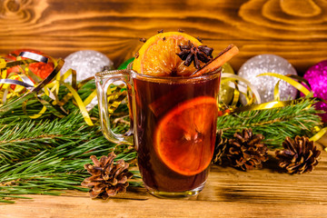 Cup of mulled wine with cinnamon, christmas decorations and fir tree branches on wooden table