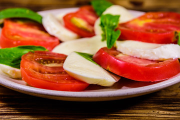 Plate with caprese salad (italian salad with cherry tomatoes, mozzarella cheese and basil leaves) on wooden table