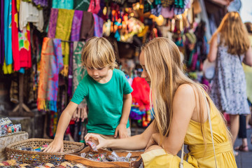 Mom and son travelers choose souvenirs in the market at Ubud in Bali, Indonesia