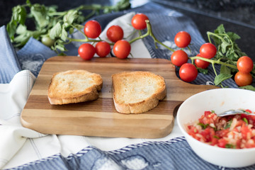 Ingredients for making a bruschetta, with rustic bread, cherry tomatoes, parsley and onion with olive oil on the wooden board. Variation of a  traditional italian appetizer or snack, antipast