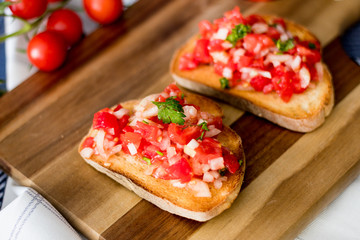Bruschetta with rustic bread, cherry tomatoes, parsley and onion with olive oil on the wooden board. Variation of a  traditional italian appetizer or snack, antipasto. 