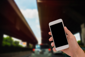 Close up hand hold mobile phone blank black screen over blurred of traffic jam on road in Bangkok Thailand.