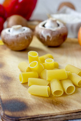 Dry rigatoni pasta on wooden kitchen board with vegetables.