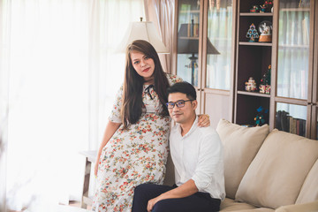 Asian male and female couples, in which men wear white shirts and women wear floral dresses, smiling while sitting on a sofa in a warm home.