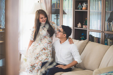 Asian male and female couples, in which men wear white shirts and women wear floral dresses, smiling while sitting on a sofa in a warm home.