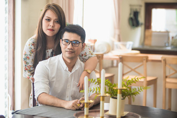 Asian male and female couples who wear white shirts and women wear floral dresses while sitting at the kitchen table.
