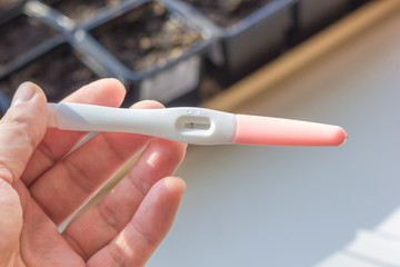 Hand holds pregnancy test over the bright background.