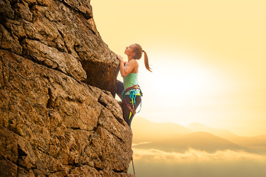 Beautiful Woman Climbing on the Rock at Foggy Sunset in the Mountains. Adventure and Extreme Sport Concept