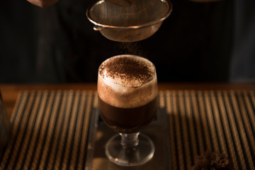 Selective focuse Close up made hot chocolate. Hand sprinkled chocolate powder on glass
