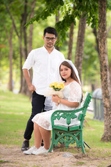 Portrait of young Asian wedding couple smiling and holding flowers in park.
