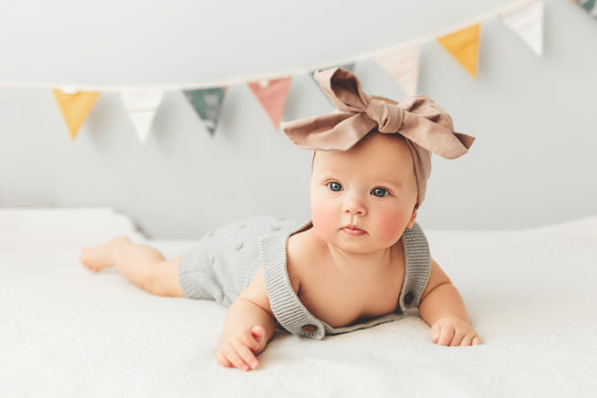 Beautiful baby lies on bed smiling bow on her head.